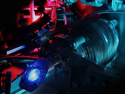 This photo shows the vacuum chamber used to measure the 2S–4P transition frequency in atomic hydrogen. The purple glow in the back stems from the microwave discharge that dissociates hydrogen molecules into hydrogen atoms. The blue light in the front is fluorescence from the ultraviolet laser that excites the atoms to the 2S state. The turquoise blue glow is stray light from the laser system used to measure the frequency of the 2S-4P transition. (Photo: MPQ)